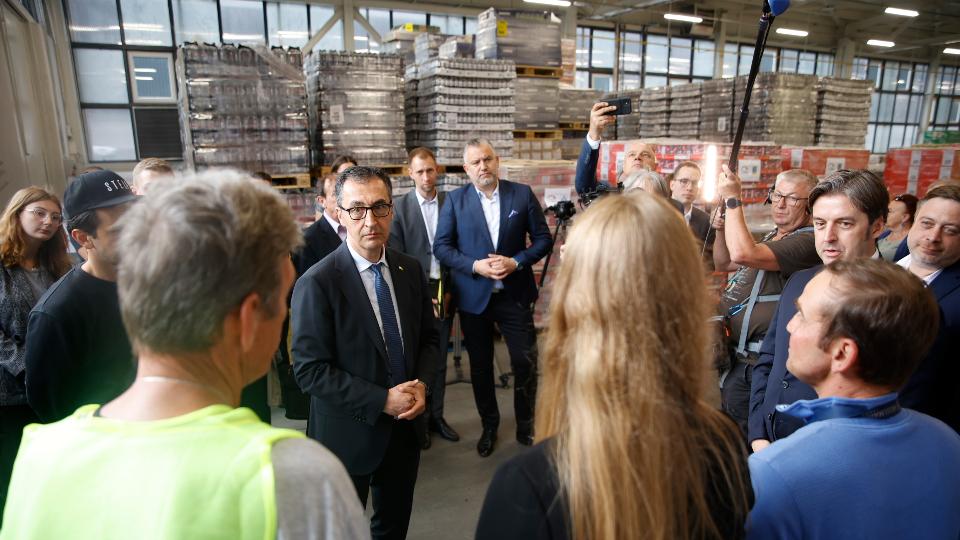 Bundesminister Özdemir im Gespräch mit Mitarbeitenden eines Lebensmittel-Hubs der German Food Bridge - dahinter Paletten mit Lebensmitteln.