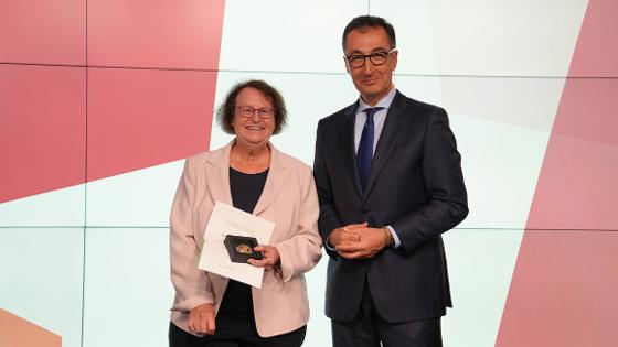 Bundesminister Özdemir steht mit Prof. Ulrike Arens-Azevêdo auf der Bühne, Prof. Ulrike Arens-Azevêdo hält die Urkunde und die Professor Niklas-Medaille in die Kamera